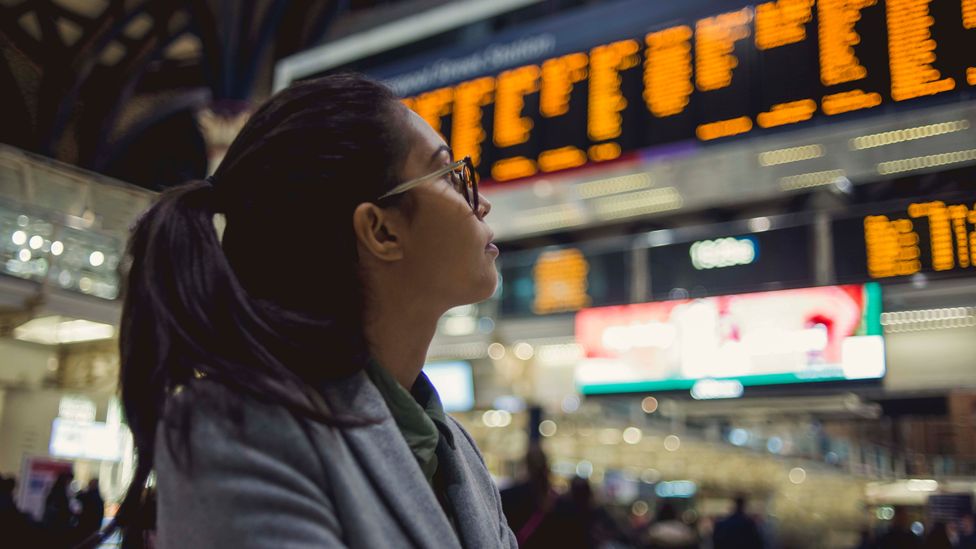 A woman looks at the train times displayed on screens in a station (Credit: Getty Images)